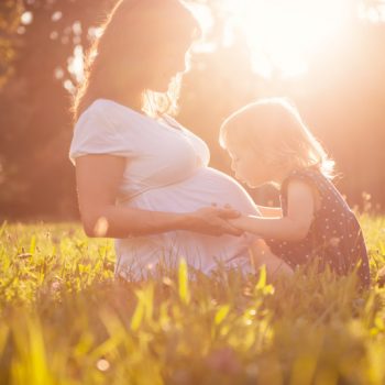 Child kissing belly og pregnant mother Little child kissing belly of her mother outdoor in sunny nature