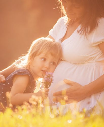 Little child listening baby in belly of her mother outdoor in sunny nature