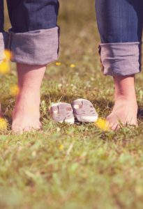 Mann und schwangere Frau stehen barfuß in der Wiese