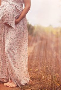 The pregnant woman in the summer in a long dress on the forest road