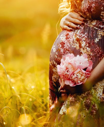 Close up of pregnant woman are relaxing in the garden at sunset. pregnant woman holding her belly and flower in the garden.
