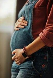 Close up of pregnant caucasian pregnant woman standing next to window and touching belly. Baby is kicking.
